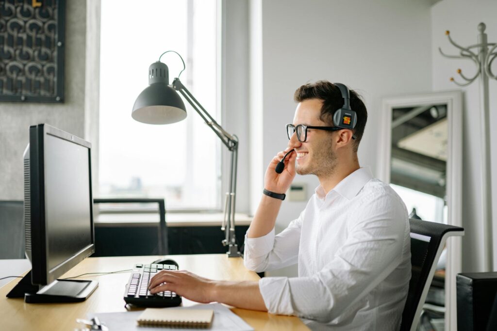 Man wearing headphones smiling while talking on the phone at a desk