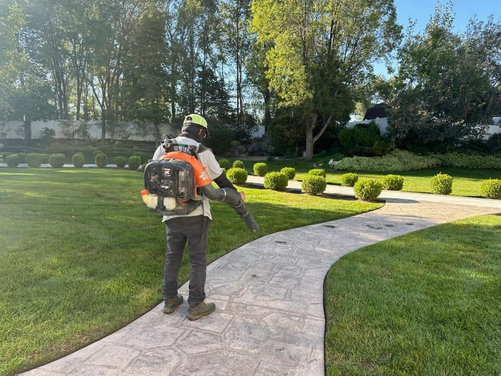 Saratoga Mowing crew performing fall cleanup in West Jordan, Utah, raking leaves and clearing debris from a residential lawn.